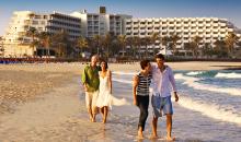 Aussicht vom Strand auf die Hotelanlage mit spazierenden Gästen im Vordergrund