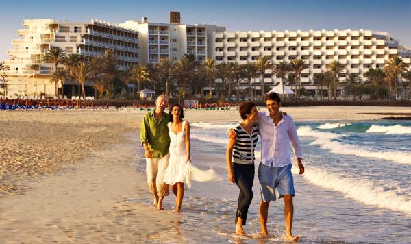 Aussicht vom Strand auf die Hotelanlage mit spazierenden Gästen im Vordergrund